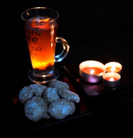 Glögilasi, pikkuleipiä ja kolme palavaa kynttilää