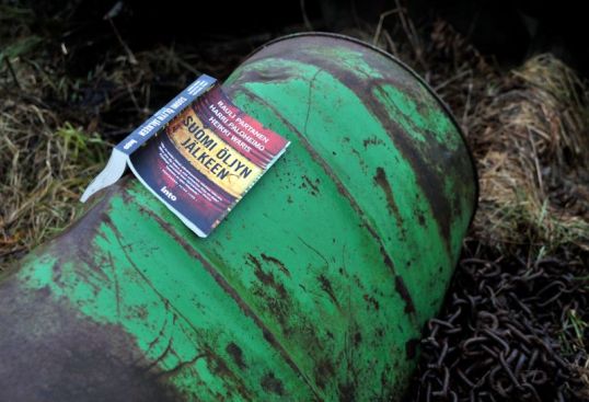 Öljytynnyri, jonka päällä on Suomi öljyn jälkeen -kirja. Vieressä ketjuja.