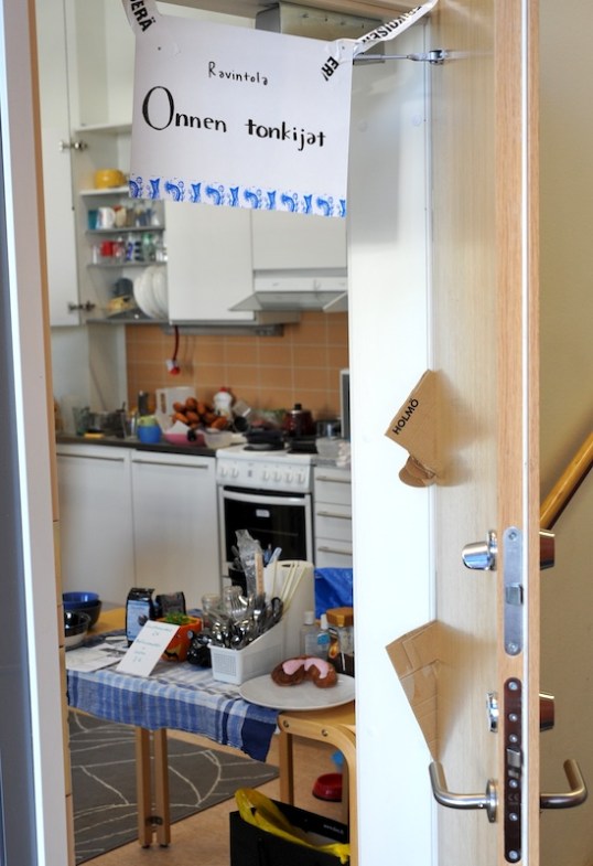 Ovi auki tilaan, jossa näkyy keittiö ja ruokailuun liittyvää välineistöä.