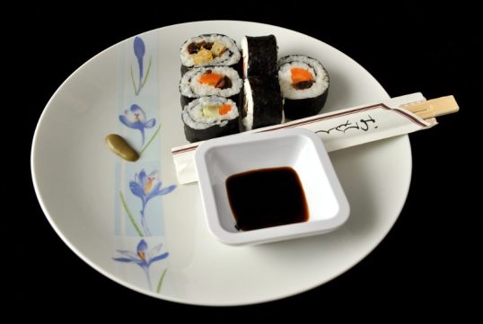 Makeja (täytteinä porkkanaa, kurkkua, herkkusieniä ja munakasta), syömäpuikot, wasabia ja kuppi soijakastiketta lautasella.