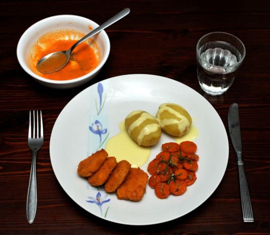 Pöydällä keittolautanen ja ruokalautanen, jolla perunoita, broilerinugetteja, porkkanoita ja keltaista kastiketta.