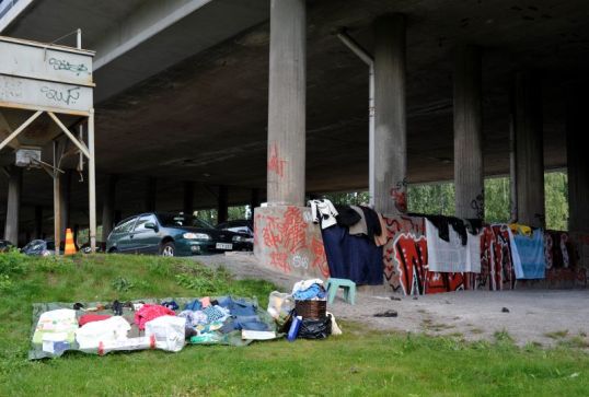 Nurmikolla vaatteita pressun päällä, sillan alla vaatteita suihkuverhojen päällä, graffitien lomassa.