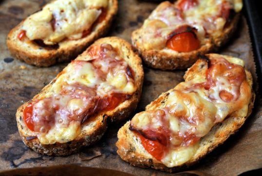 Uunipellillä sekaleipäviipaleita. joiden päällä juustoa, serranonkinkkua ja tomaattia.