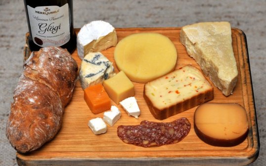 Puisella tarjottimella glögipullo, leipä, leikkeitä ja monenlaisia juustoja.