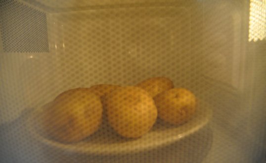 Perunoita lautasella kypsymässä mikroaaltouunin sisällä.