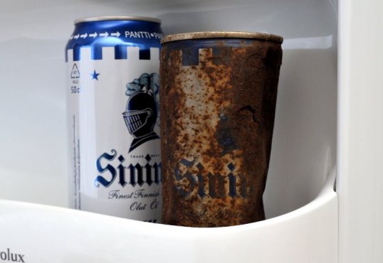 Ruostunut oluttölkki ja vastaava alumiinitölkki jääkaapin ovessa.
