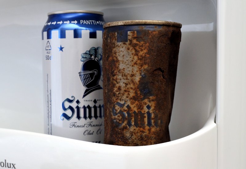 Ruostunut oluttölkki ja vastaava alumiinitölkki jääkaapin ovessa.