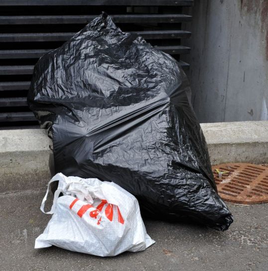 Täysi jätesäkki asvaltilla pienen muovipussin vieressä.