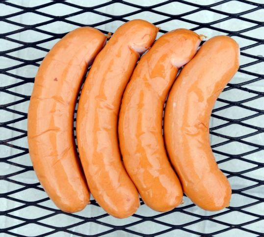 Neljä makkaraa metalliritilän päällä.