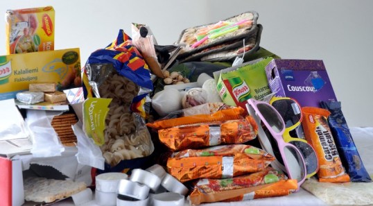 Kasassa liemikuutioita, voileipäkeksejä, näkkileipä, tuikkukynttilöitä, sipsejä, pähkinöitä, valkosipuleita, pikanuudelipusseja, aurinkolaseja, pussikastikepakkaus, patalappuja, kakkukynttilöitä, kuskusrasia ja suklaapatukoita.