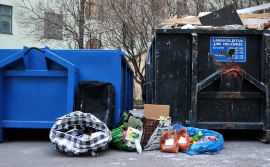 Kahden jätelavan edessä muovisia kestokasseja, joista pursuaa ruokapakkauksia.