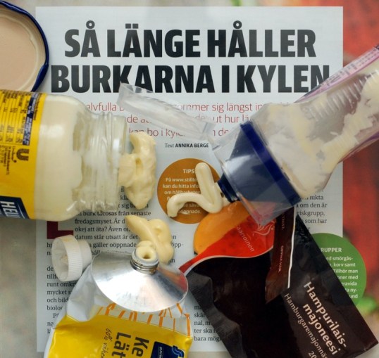 Lehtiartikkelin päällä lasipurkista, muovisesta pursotinpurkista, muovipussukasta ja metalliputkilosta ulos tullutta majoneesia.