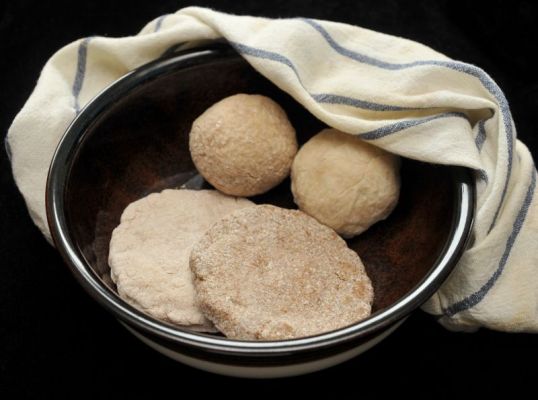 Kaksi sämpylää ja kaksi ohutta leipää Kermansaven kulhossa, jonka ympärillä on siniraidallinen liina.