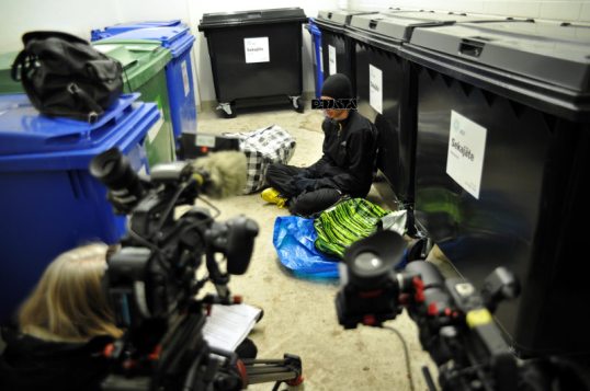 Onni Tonkija jätehuoneen lattialla kahden videokameran ja haastattelijan edessä.