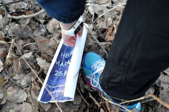 Lenkkeilijä poimii mainosjulisteen maahan pudonneiden lehtien päältä.