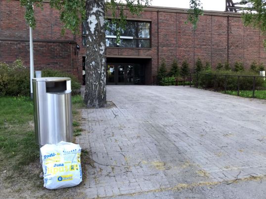 Valkoinen muovikassi roskakorin vieressä Oulunkylän kirkon edessä.