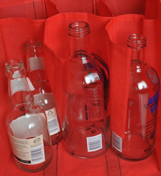 Punaisessa, lokeroidussa pullokassissa kaksi pientä siideripulloa ja kaksi isoa votkapulloa.