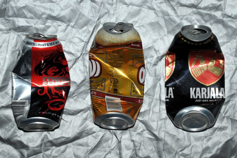 Kolme keskeltä litistynyttä tölkkiä hopeanvärisen peitteen päällä.