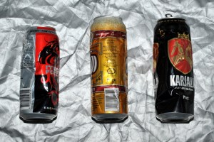 Kolme lommoista juomatölkkiä hopeanvärisen peitteen päällä.