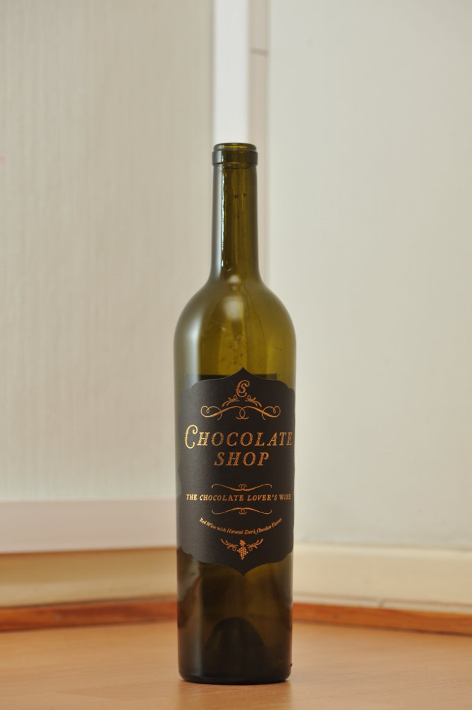 Tyhjä Chocolate Shop -punaviinin 0,75 litran vihreä lasipullo puunvärisellä lattialla.