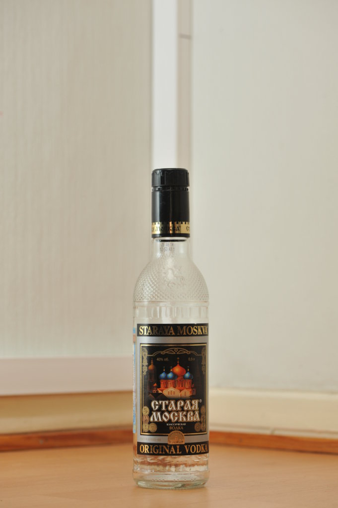 Tyhjä Staraja Moskva (Старая Москва) -votkan 0,5 litran kirkas lasipullo puunvärisellä lattialla.