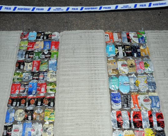 Suojatiellä valkoisten raitojen välissä litistyneitä juomatölkkejä. Taustalla poliisin sulkunauhaa.