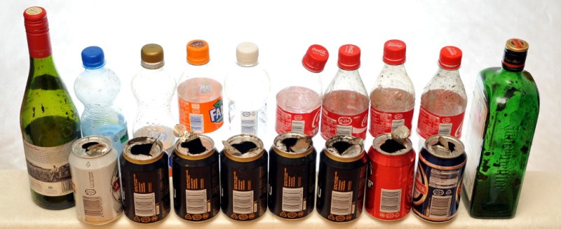 Lasipulloja sekä osittain avattuja muovipulloja ja juomatölkkejä, joiden sisäreunoilla näkyy tupakan jäämiä.