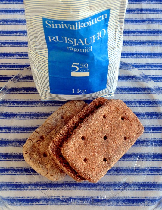 Kaksi ruispalaleipää mikron lasilautasella. Takana T-kaupan Sinivalkoinen-ruisjauhopussi ja taustalla sini-valkoraitainen kangas.