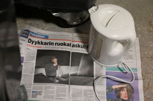 Helsingin Uutiset auki dyykkarijutun kohdalta jätekatoksen lattialla vedenkeittimen alla.