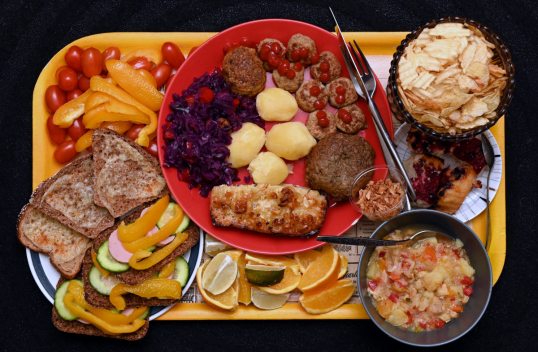 Keltaisella tarjottimella pikkutomaatteja, suikaloitua paprikaa, lämpimiä juustoleipiä, kurkku-paprika-maksamakkararuisleipiä, appelsiini- ja limettilohkoja, lautasellinen broilerikeittoa, paahdettua sipulia, marjapiirakkaa, sileitä ja poimutettuja perunalastuja, lihapullia ja ketsuppia, lihamurekepihvi, keitettyjä perunoita, punakaalisalaattia ja liha-makaronilaatikkoa.