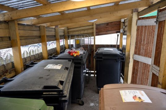 Jätekatoksessa vieri vieressä roska-astioita, joista yhden päällä on klementiinejä, palanen paprikaa ja leipäpussi.