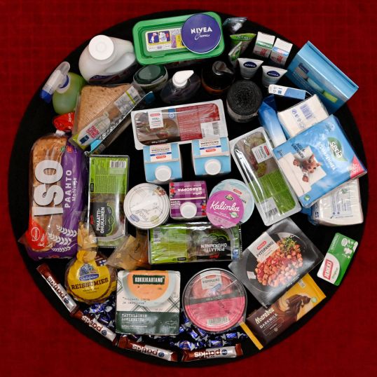 Ympyrän muotoisessa asetelmassa muun muassa suklaata, valmisruokia, leipää, maitotuotteita, pesuaineita, puhdistusliinoja, roskapusseja ja nenäliinoja.