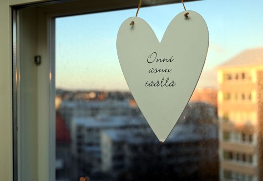 Ikkunassa valkoinen sydän, jossa lukee ”Onni asuu täällä”.