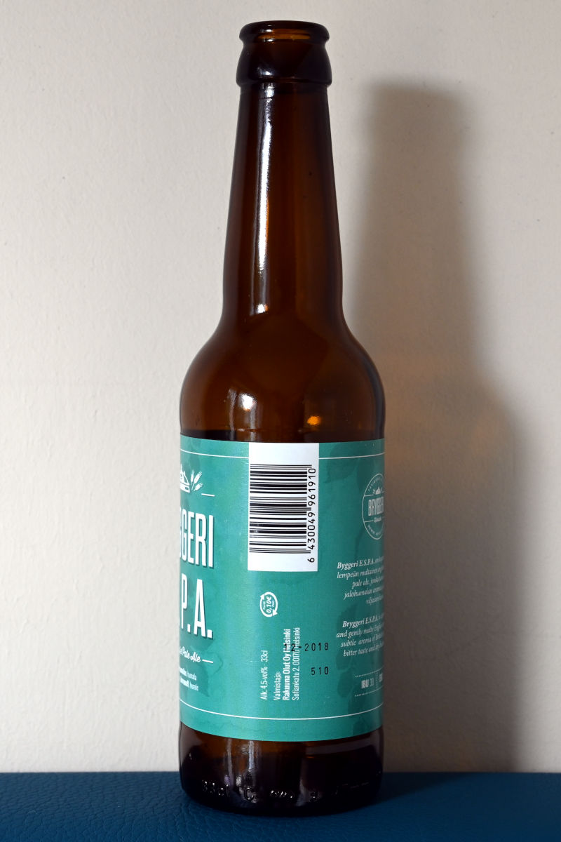 Bryggeri E. S. P. A. -olutpullossa hyvin pieni suomalainen panttimerkki isohkon tyhjän tilan ympärillä.