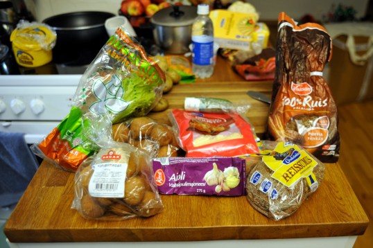 Pöydällä lehtisalaattia, leivonnaisia, kurkkua, juustoraastetta, majoneesiputkilo ja ruisleipää.