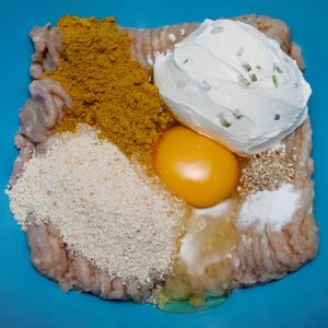 Turkoosissa kulhossa kalkkunan jauhelihaa, tuorejuustoa, rikottu kananmuna, korppujauhoja, karria, suolaa ja pippuria.