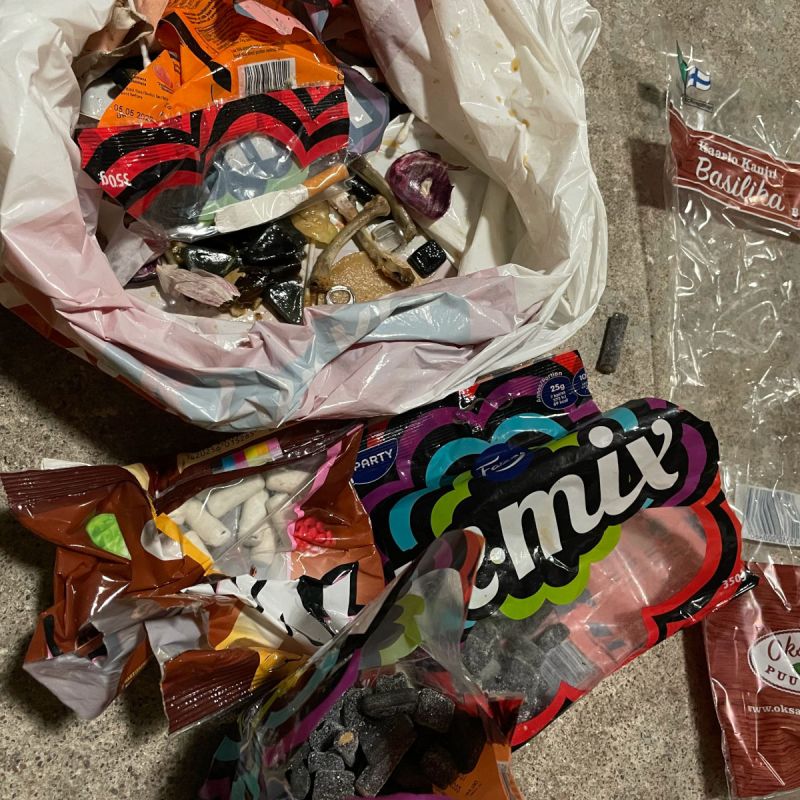 Roskapussi ja siitä kaivettuja makeispusseja, joiden pohjalla on salmiakkia ja liitulakuja.